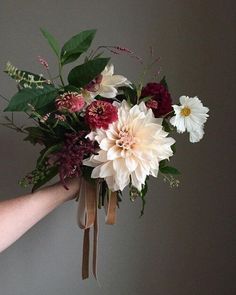 a bouquet of flowers is being held up by someone's hand with ribbon around it