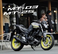 a yellow and black motorcycle parked on the street in front of a building with people walking by