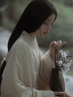 a woman holding a vase with flowers in it and looking down at the ground below