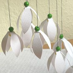 four white paper flowers hanging from strings on a table with a wall in the background