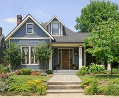 a blue house with flowers and trees in the front yard