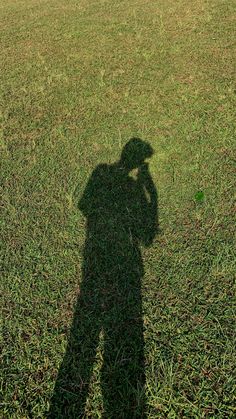 the shadow of a person holding a frisbee in their hand and standing on grass