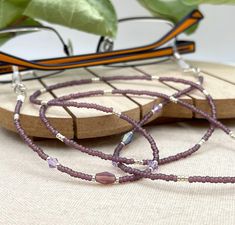 Dramatic and bohemian eyeglass necklace chain in matte purple and rainbow tones made with Preciosa Czech crystal seed beads and purple cubic zirconia charms.      Paired with beautiful and delicate purple charms, this handmade eyeglass chain will definitely create a unique look. This eyeglass lanyard is made on strong quality beading wire with silver plated wire guardians that protect the eyeglass holder grips. The necklace is ended with spring clasps that hold the eyeglass grips and they can be easily removed to transform the necklace into a mask holder. FREE Shipping for additional items  ~ All items are beautifully packed ready to give as a gift and carefully wrapped up to ensure a safe delivery.   ~ The environment is very important for us therefore, in order to reduce waste, we will p Adjustable Purple Glass Glasses Chains, Adjustable Purple Glass Beaded Necklaces, Handmade Purple Glass Beaded Necklaces, Adjustable Lavender Beaded Necklaces, Purple Glass Glasses Chains As Gift, Beaded Sunglasses Chain, Purple Charms, Eyeglass Chain Holders, Glasses Lanyard