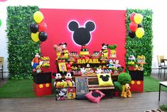 mickey mouse birthday party setup with balloons and decorations on the wall behind it, surrounded by fake trees