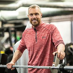 a man in a red shirt is holding a barbell and smiling at the camera