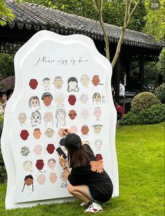 a woman is drawing on a sign with many people's faces in different colors