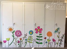 a white cabinet with colorful flowers painted on the front and back doors, in a room with carpeted flooring