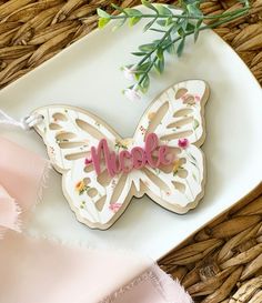 a white plate topped with a butterfly shaped cookie next to a pink ribbon and flowers