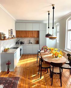 a kitchen and dining room with hardwood floors, white cabinets and wooden table surrounded by chairs