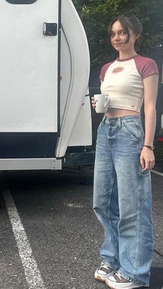 a woman standing in front of a trailer with her hand on her hip and holding a coffee cup