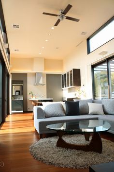 a living room filled with furniture next to a window covered in lots of windows and a ceiling fan