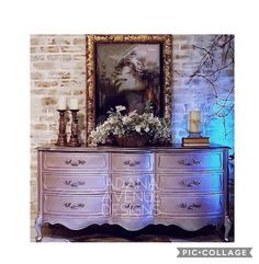 an ornate dresser with flowers and candles on it in front of a brick wall, next to a painting