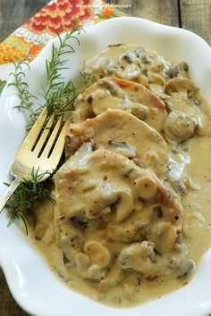 a white plate topped with meat covered in gravy next to a knife and fork