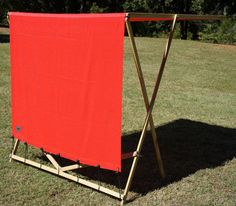 a red towel is hanging on a clothes rack in the grass near some trees and bushes