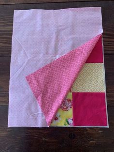 a pink and yellow patchwork quilt on top of a wooden floor next to a piece of cloth