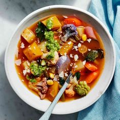 a white bowl filled with vegetable soup on top of a blue towel next to a spoon