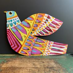 a colorful bird sitting on top of a wooden table next to a blackboard wall