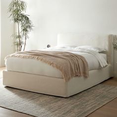 a white bed sitting on top of a wooden floor next to a potted plant