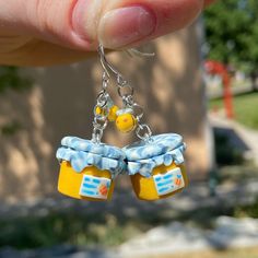 a pair of yellow and blue earrings hanging from a persons hand in front of a building