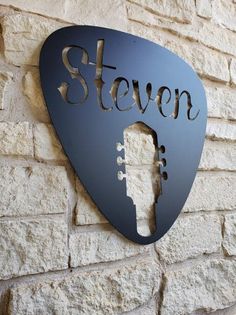 a metal guitar picker is mounted to the side of a brick wall that reads,'seven '