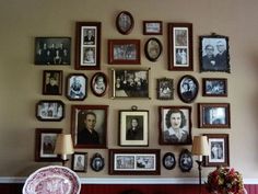 a wall with many framed pictures on it and a chair in front of the table