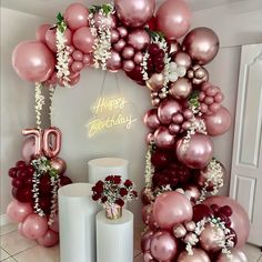 balloons and flowers are arranged in front of a birthday arch