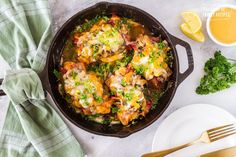 a skillet filled with chicken and vegetables on top of a white plate next to silverware