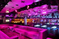 the interior of a nightclub with pink lighting and purple couches in front of tables