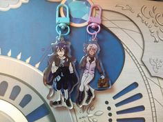 two anime key chains are hanging on a clock