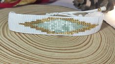 a white and gold beaded bracelet sitting on top of a wooden table next to a stuffed animal