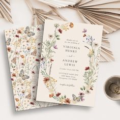 two wedding cards on top of each other with flowers and butterflies in the middle, next to an open book