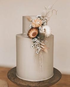 a three tiered cake with flowers and feathers on the top is sitting on a wooden stand