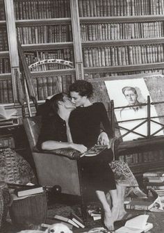 black and white photograph of two people sitting in a chair with bookshelves behind them