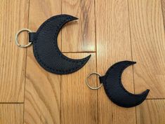 two black leather moon keychains sitting on top of a wooden floor