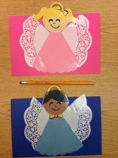 two paper angel cards sitting on top of a wooden table next to a crayon pencil