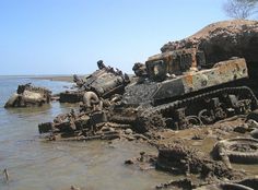 an old rusted tank sitting on top of a beach next to the ocean and rocks