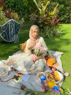 a woman sitting on top of a blanket in the grass with food and drinks around her