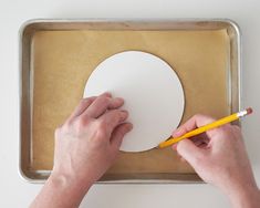 a person is using a pencil to cut out a paper circle on a baking sheet