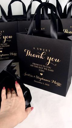 a woman's hand holding onto some black bags with gold foil lettering on them