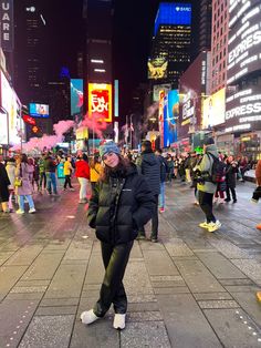 a woman standing in the middle of a busy city street at night with lots of people