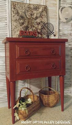 a red table with two baskets on it and an old wall hanging above the top