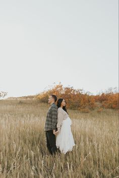 a man and woman standing in the middle of a field with tall grass on each side