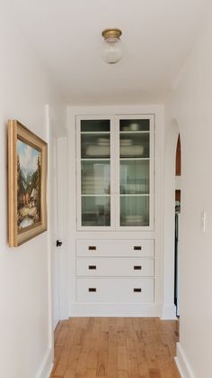 an empty room with white cabinets and wood flooring in front of a painting on the wall