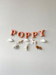 the word poppy spelled out with toy animals hanging from strings in front of a white wall