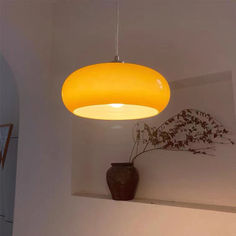 a yellow light hanging from the ceiling above a vase with flowers in it on a shelf