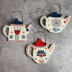 three ceramic teapots are hanging from hooks on the wall, decorated with flowers and hearts