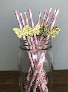 several pink and white striped straws in a mason jar with gold glitter butterfly decorations