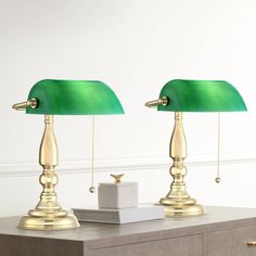 two green lamps sitting on top of a table next to a white box with a gold ring