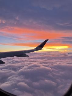 the wing of an airplane as it flies above the clouds at sunset or dawn in the sky