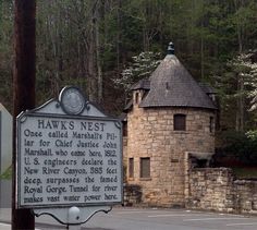 a sign in front of a stone building with a clock on it's face